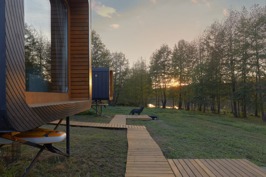 Two BRO6 cabins with illuminated windows beside a boardwalk at dusk