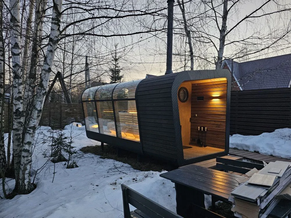 Built panoramic sauna with a rounded profile and dark exterior in a snowy setting