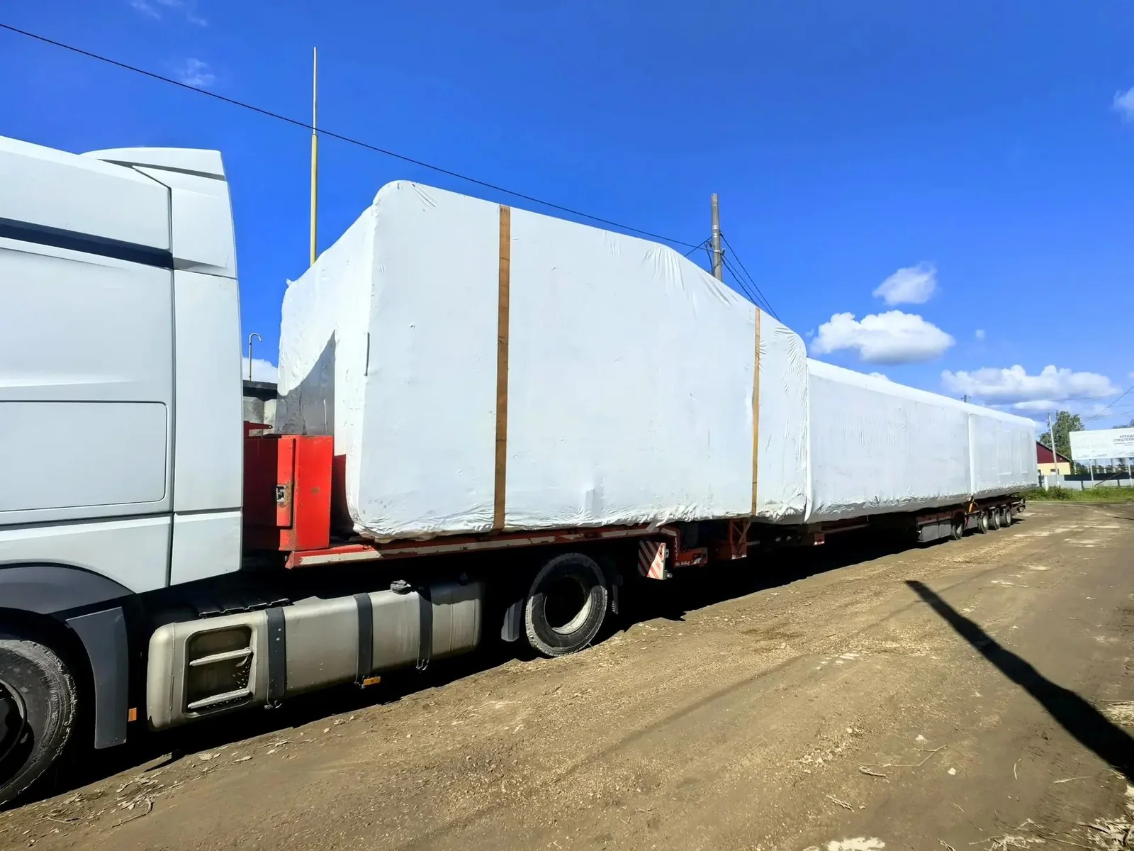 Wrapped wooden cabin modules secured on a transport trailer under a blue sky