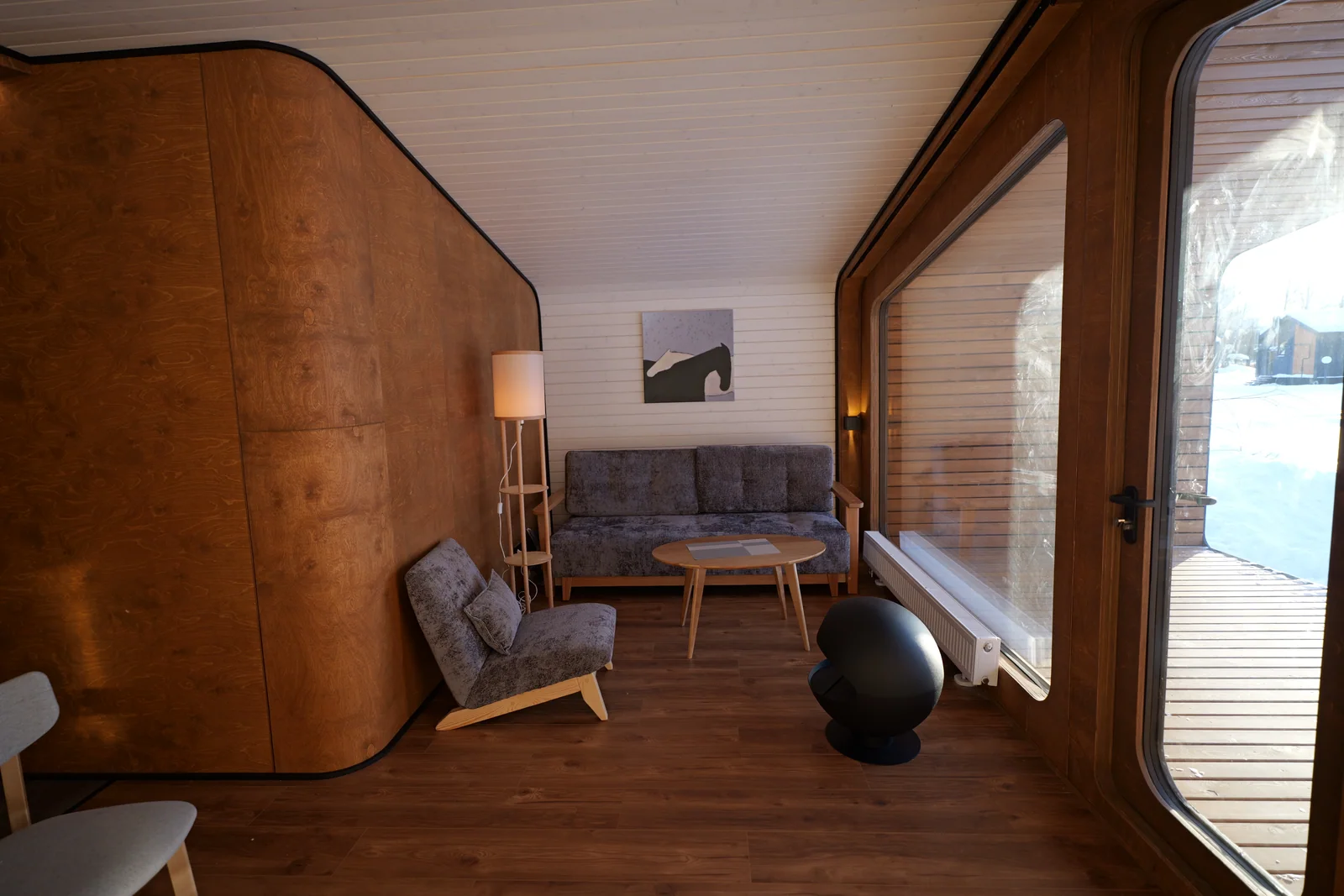 Compact wooden-cabin living area with a sofa, table and full-height opening