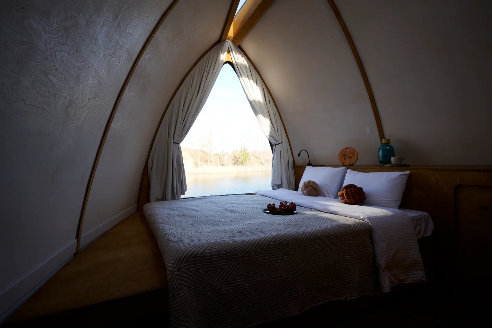 Bed inside a curved wooden pod with a triangular end opening